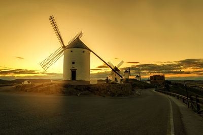 Traditional windmills by road against sky during sunset