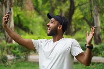 Young man with arms outstretched standing against trees