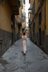 Rear view of woman walking on alley amidst buildings