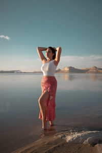 Full length of woman standing at beach against sky during sunset