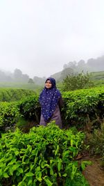 Portrait of young woman standing on field against sky