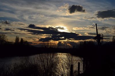 Silhouette trees by river against sky during sunset