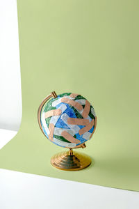 Round shaped globe of planet earth plastered with numerous medical band aids placed on light green background