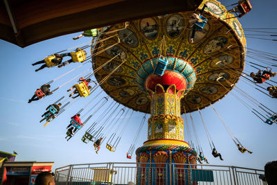 Low angle view of chain swing ride against sky at amusement park during golden hour. 