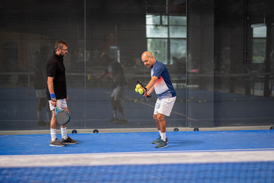 Monitor teaching padel class to man, his student - trainer teaches boy how to play padel on indoor 