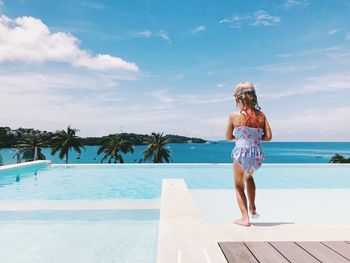 Rear view of girl standing at infinity pool