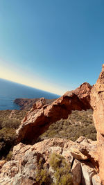 Rock formation by sea against clear blue sky