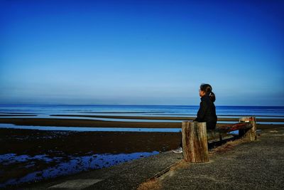 Girl looking at sea against blue sky