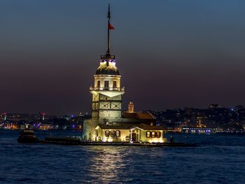 Illuminated building by sea against sky at night