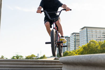 Cropped unrecognizable young male riding bmx bike on edge of border on sunny weekend day on city street in summer