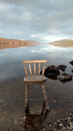 Deck chairs on rocks by sea against sky