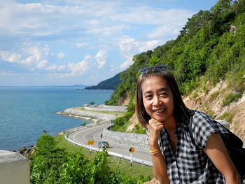 Portrait of young woman standing by sea against mountain