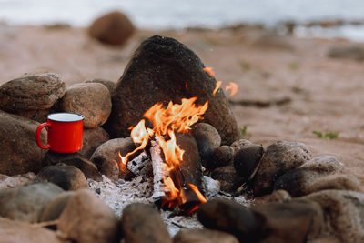 Close-up of rocks on beach, campfire in nature and a red cup with coffee or tea