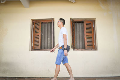 Full length portrait of young woman standing against wall