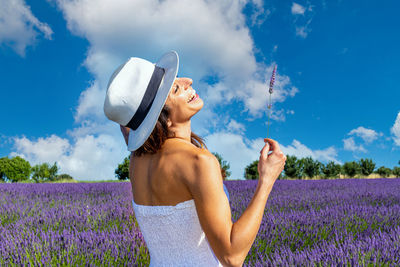 Happy young woman plays with her hat and a lavender spring in a blooming field. 