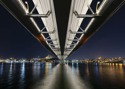 Illuminated bridge over river against sky at night