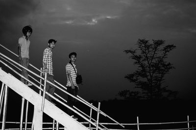 Portrait of men with friend walking on steps against sky at night