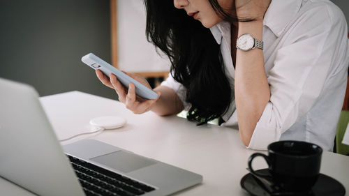 Midsection of woman using mobile phone while sitting on table