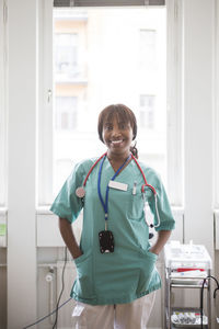 Portrait of mature female healthcare worker with hands in pockets standing in clinic