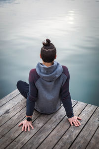 Rear view of woman sitting on pier over lake