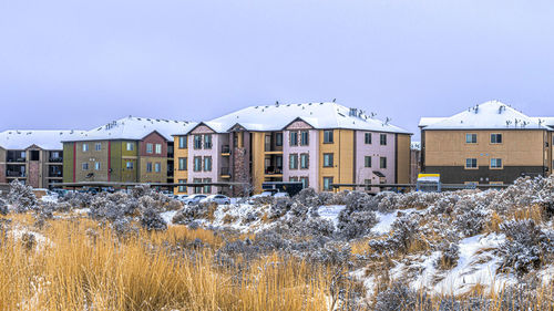 Houses on snow covered field by buildings against sky