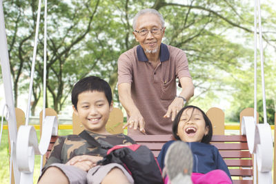 Happy siblings with grandfather swinging in playground