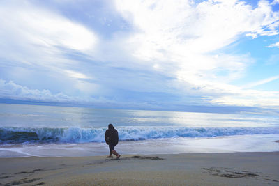 Rear view of man standing on beach against sky