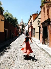 Rear view of woman standing on footpath amidst buildings