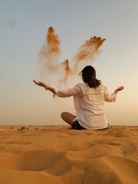 Rear view of woman sitting on sand at desert