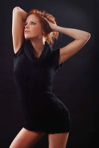 Young woman looking away while standing against black background