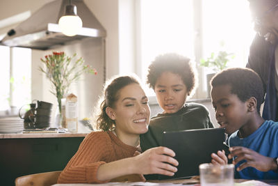 Smiling mother watching digital tablet with sons at home