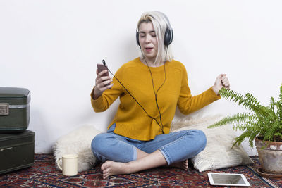 Portrait of young woman using mobile phone while sitting against white background