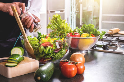 Midsection of woman making vegetable salad in bowl on kitchen counter