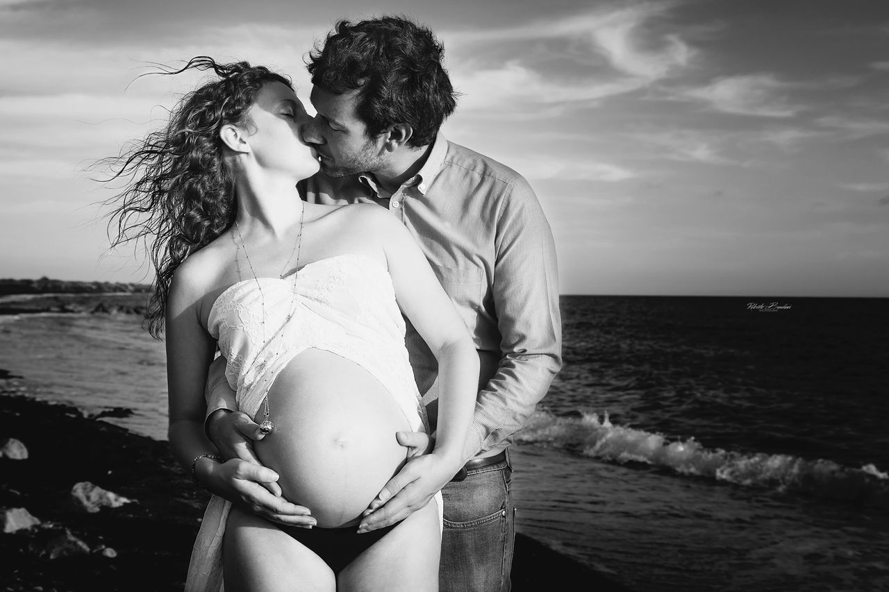 sea, water, two people, sky, togetherness, pregnant, young adult, women, land, young women, nature, love, bonding, adult, lifestyles, couple - relationship, positive emotion, real people, three quarter length, horizon over water, hands on stomach, hairstyle, outdoors