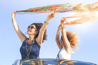 Low angle view of woman holding umbrella against blue sky