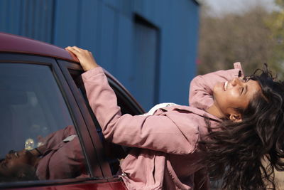 Side view of carefree woman leaning out from car window