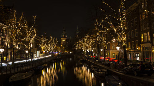 Illuminated bridge over canal by buildings in city at night