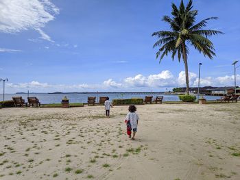 Rear view of people walking at beach against sky