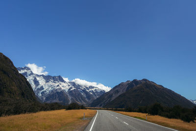 Road leading towards mountains against clear blue sky