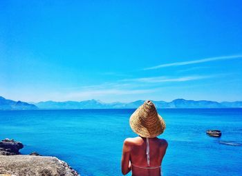 Rear view of woman wearing hat while standing against sea at beach