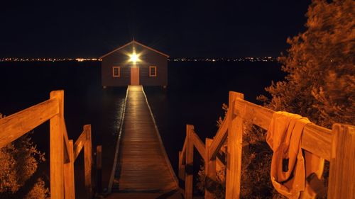 Illuminated pier amidst sea against sky at night