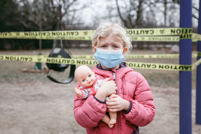 Portrait of cute girl wearing mask holding doll while standing park