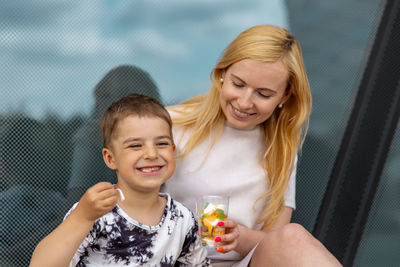 Happy blond woman and little boy sitting on terrace and eating sweets. mother and son enjoy