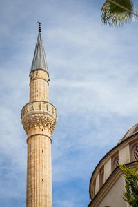 Image of a stone beige tower of a mosque on against the sky in a warm hot country with palm trees
