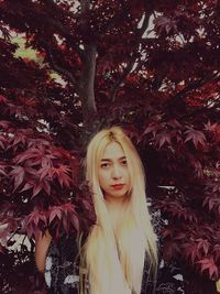 Portrait of beautiful young woman standing by tree during autumn