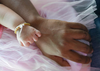 Close-up of baby and woman hand on bed