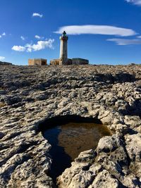 Lighthouse on landscape against cloudy sky