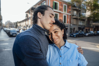 Young man with eyes closed arm around of girlfriend on street