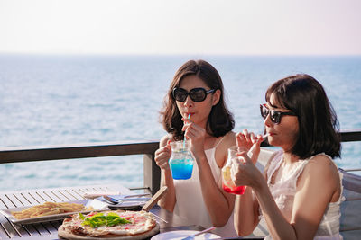 Friends drinking juices at restaurant by sea during sunny day