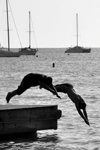 Friends diving into river against moored sailboats